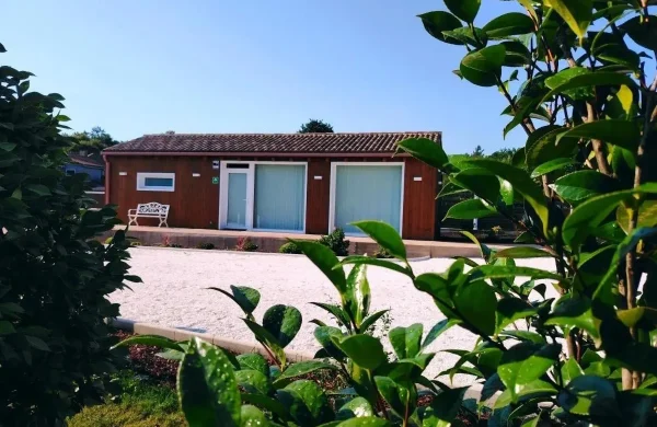 Cabaña de madera de una planta con acceso a nivel, vista entre las camelias del jardín