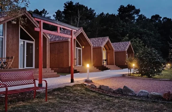 Cabañas de madera iluminadas al anochecer con pérgola roja, Valle de Mahía