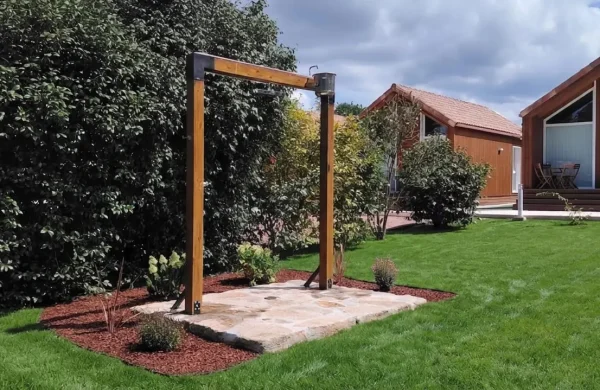 Ducha exterior de madera sobre losas de piedra en el jardín de las cabañas, Brión